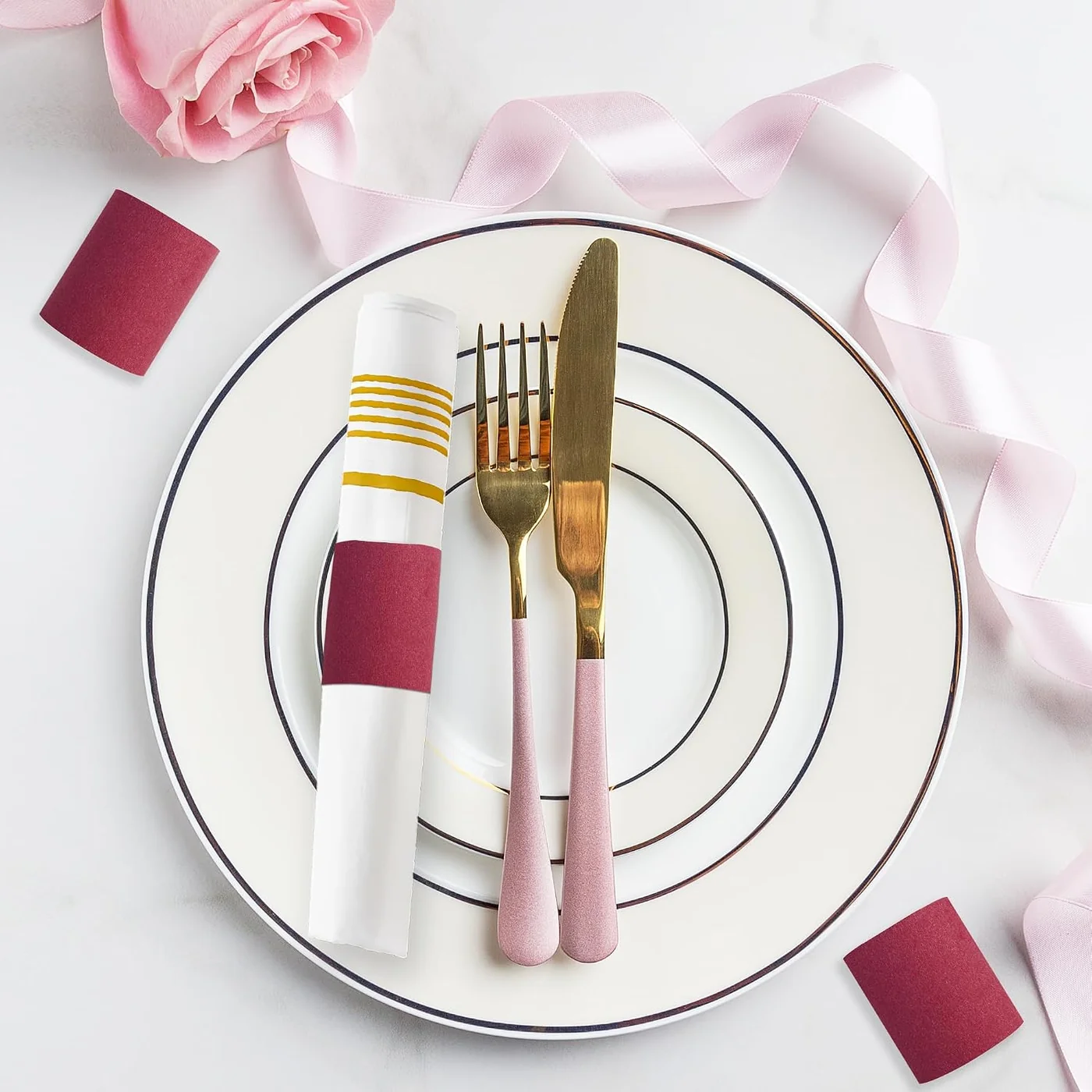 Burgundy napkin band around a white napkin beside pink-handled flatware on a layered white plate